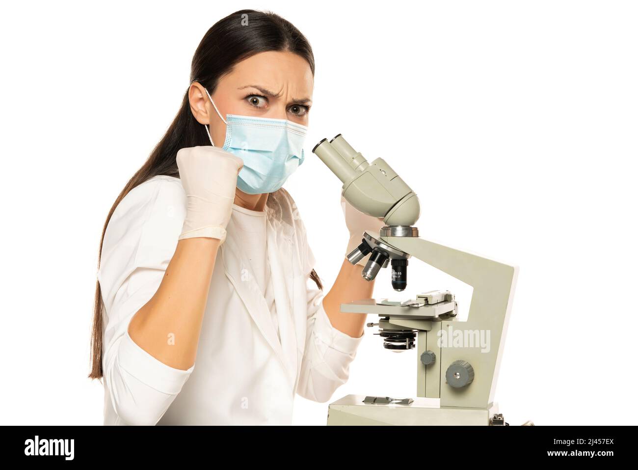 Scienziata nervosa femminile arrabbiata con maschera protettiva e microscopio, sfondo bianco. Foto Stock