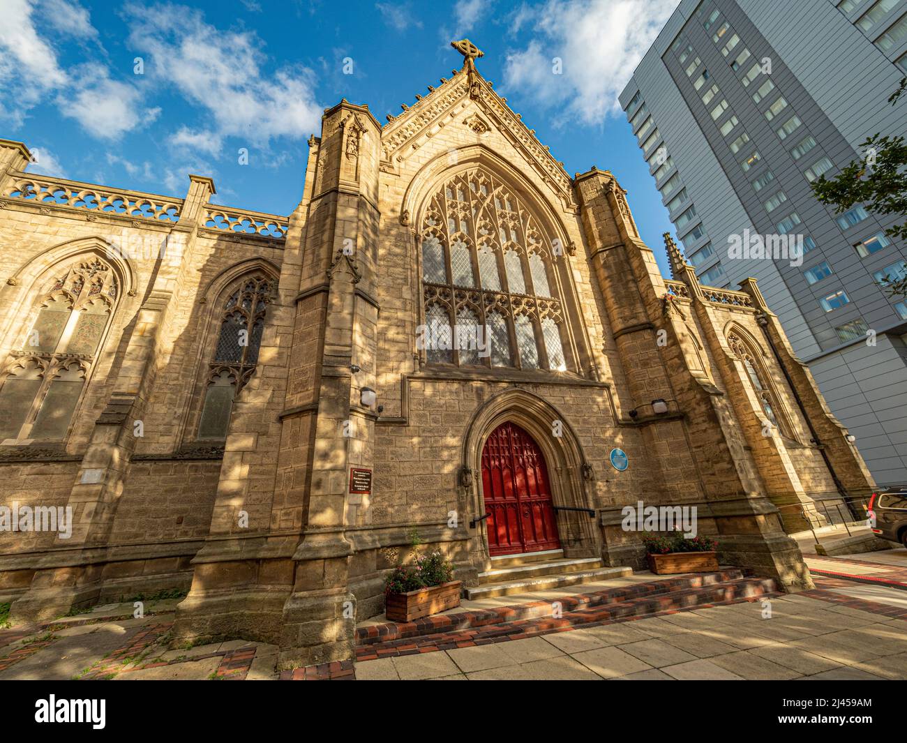 Facciata ovest della Mill Hill Chapel, con le sue porte rosse luminose e un moderno edificio a più piani alle spalle Foto Stock