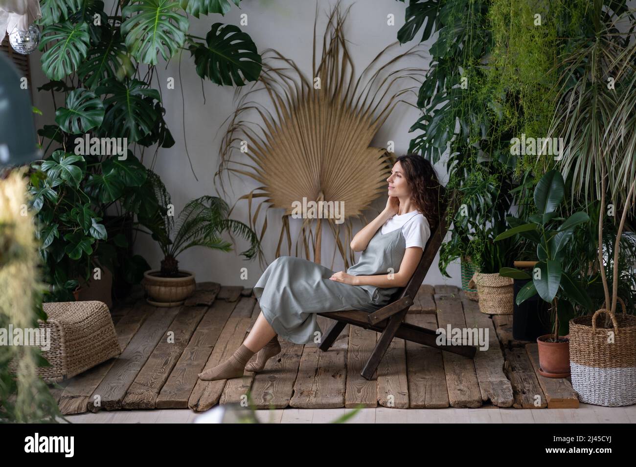 Giovane donna rilassata sedersi su una comoda poltrona in un elegante giardino interno con piante esotiche verdi Foto Stock