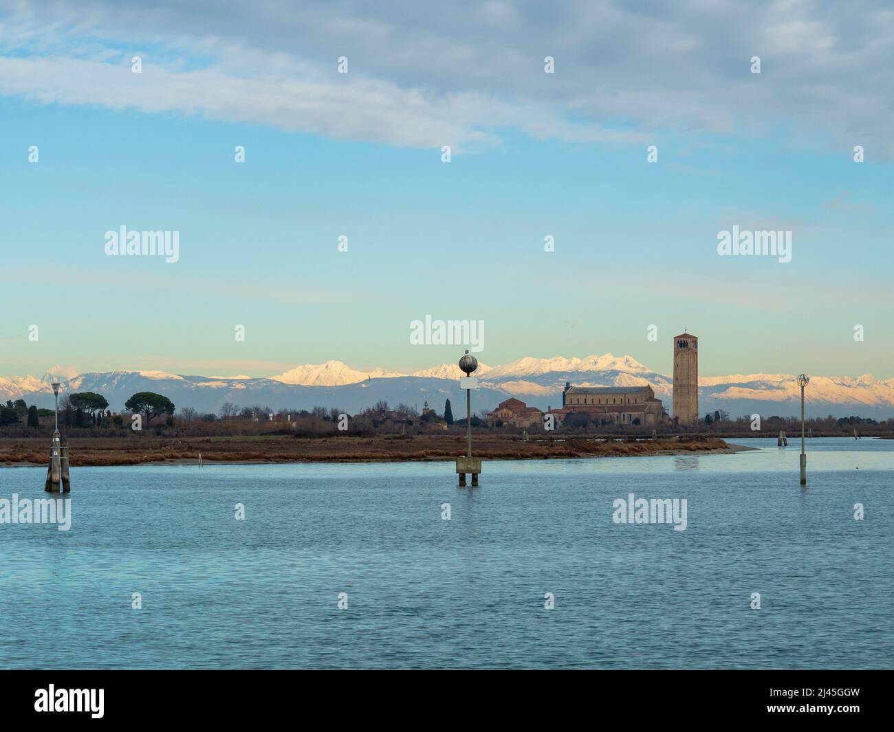 Vista da Burano verso l'isola di Torcello e la chiesa di Santa Maria Assunta con le montagne dolomitiche innevate - Italia Foto Stock