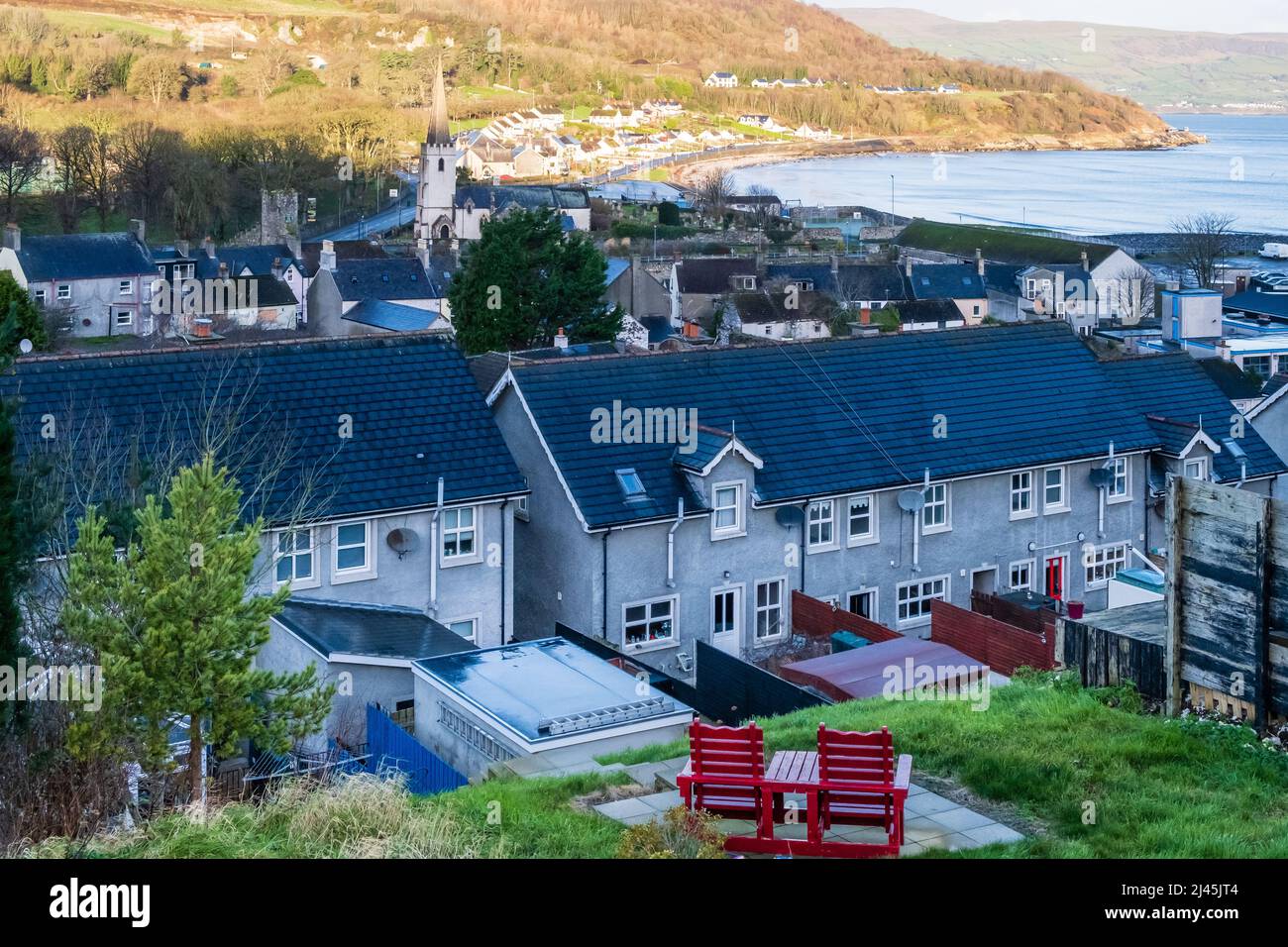 Due sedie rosse su un patio pavimentato con pittoresche vedute della cittadina costiera di North Antrim di Glenarm, nell'Irlanda del Nord. Foto Stock