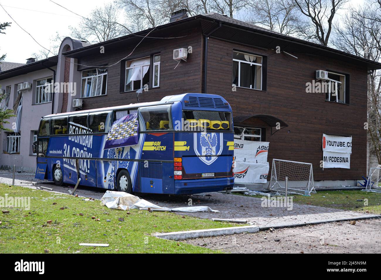 CHERNIHIV, UCRAINA - 11 APRILE 2022 - Un autobus danneggiato del FC Desna Chernihiv rimane presso un edificio con finestre schiacciate vicino al Chernihiv Olympic Sport T. Foto Stock