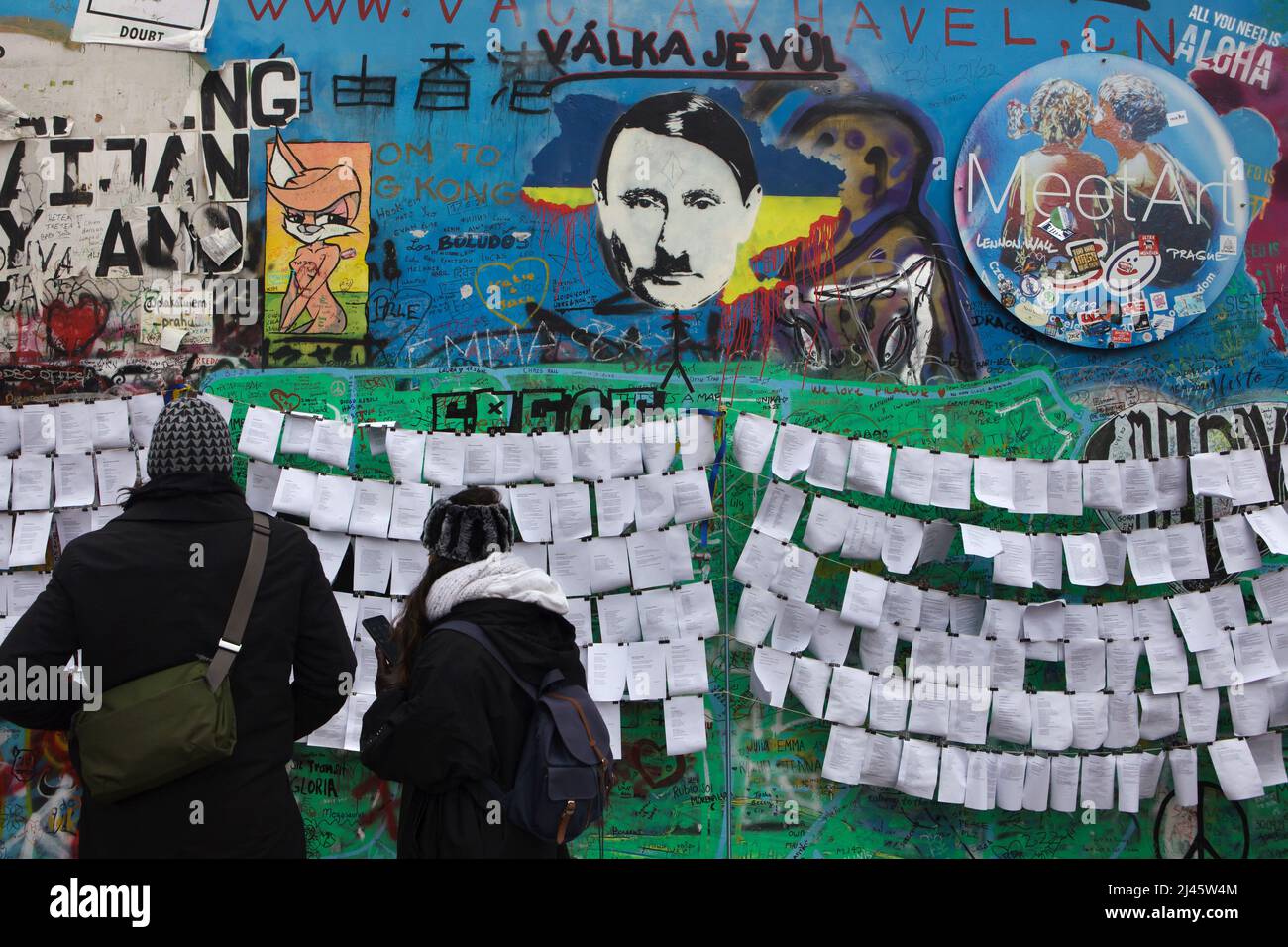il presidente russo Vladimir Putin ha raffigurato il muro di Lennon (Lennonova zeď) a Praga, Repubblica Ceca. Il presidente Vladimir Putin è raffigurato con i caratteristici baffi da taglio e da spazzolino di Adolf Hitler collocati sulla sanguinosa mappa dell'Ucraina per protestare contro l'invasione russa dell'Ucraina nel 2022. L'iscrizione ceca sul capo di Putin 'Válka je vůl' (letterario significa: La guerra è un bue) è una linea di una canzone popolare della rock band ceca 'Synkopy 61'. I turisti nella foto del 2 aprile 2022 leggono i testi antguerra posti accanto al Muro di Lennon. Foto Stock