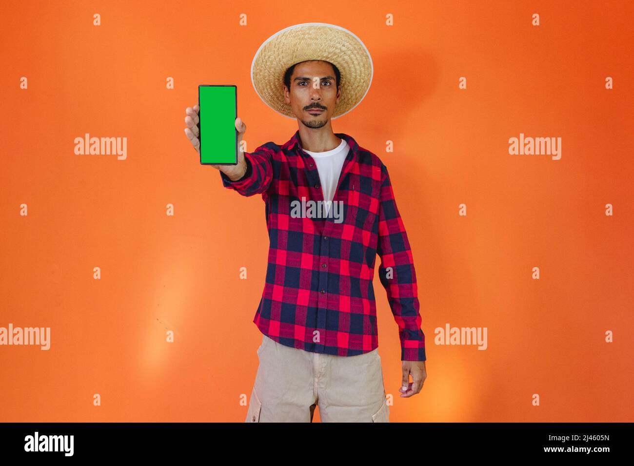 Black Man con Junina Party vestito con un tablet o cellulare isolato su sfondo arancione. Giovane uomo che indossa abiti tradizionali per Festa Junina - Foto Stock