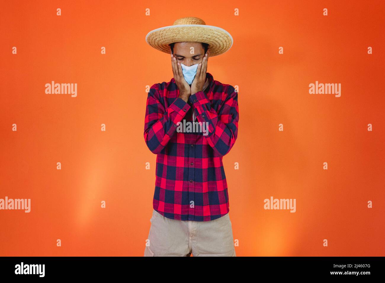 Black Man con Junina Party vestito isolato su sfondo arancione. Giovane uomo che indossa abiti tradizionali per Festa Junina - Festival brasiliano di giugno. Foto Stock