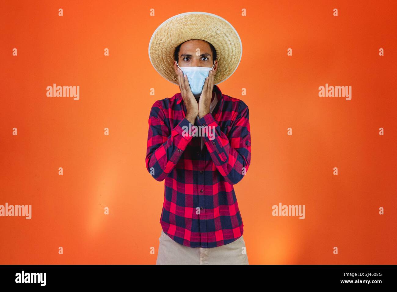 Black Man con Junina Party vestito isolato su sfondo arancione. Giovane uomo che indossa abiti tradizionali per Festa Junina - Festival brasiliano di giugno. Foto Stock