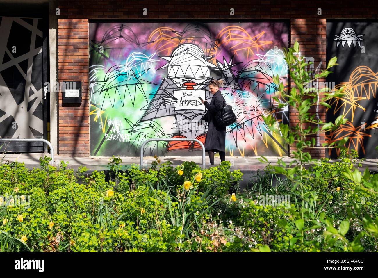 Pedone, donna persona camminare accanto graffiti murale opere d'arte su un muro in Old Street Shoreditch Londra EC1 Inghilterra Regno Unito KATHY DEWITT Foto Stock