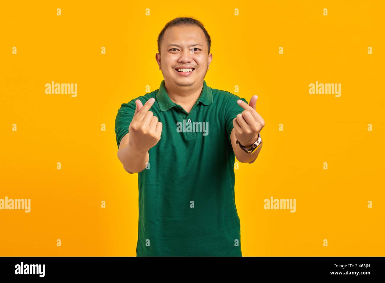 Ritratto di giovane uomo asiatico allegro mostrando il cuore dito su sfondo giallo Foto Stock