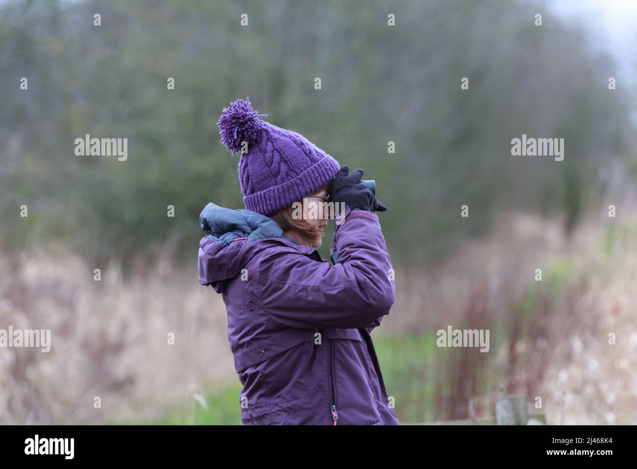 Una donna adulta singola con binocolo in cerca di uccelli e fauna selvatica Foto Stock