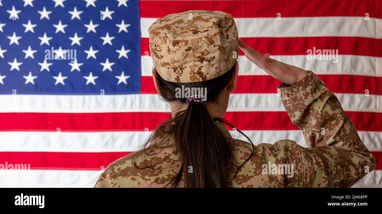 Donna US Army Soldier in piedi di fronte a una bandiera americana e saluta. Donna in uniforme militare vista posteriore Foto Stock
