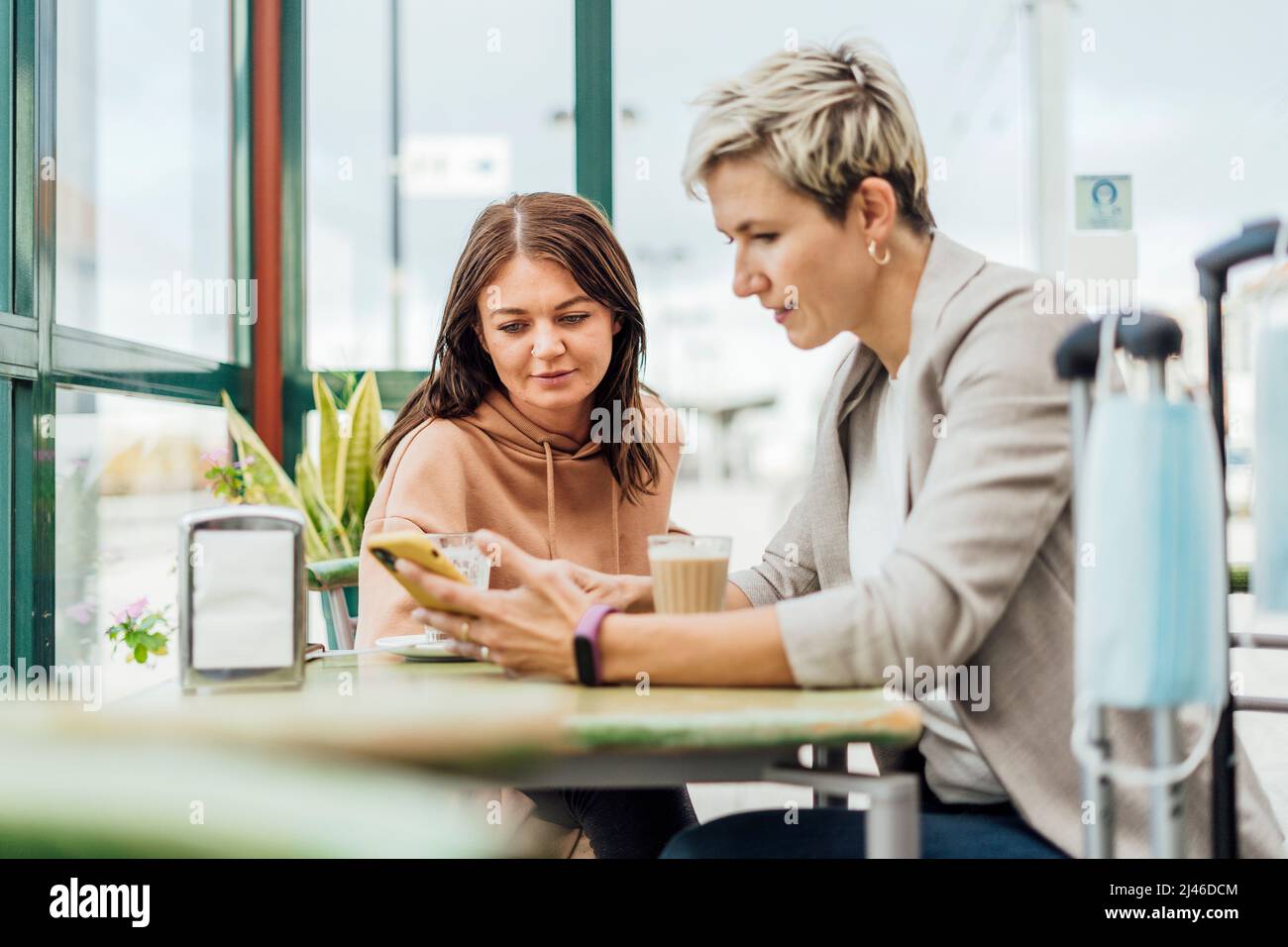 Due amiche che viaggiano in un caffè - maschera e bagagli in primo piano Foto Stock