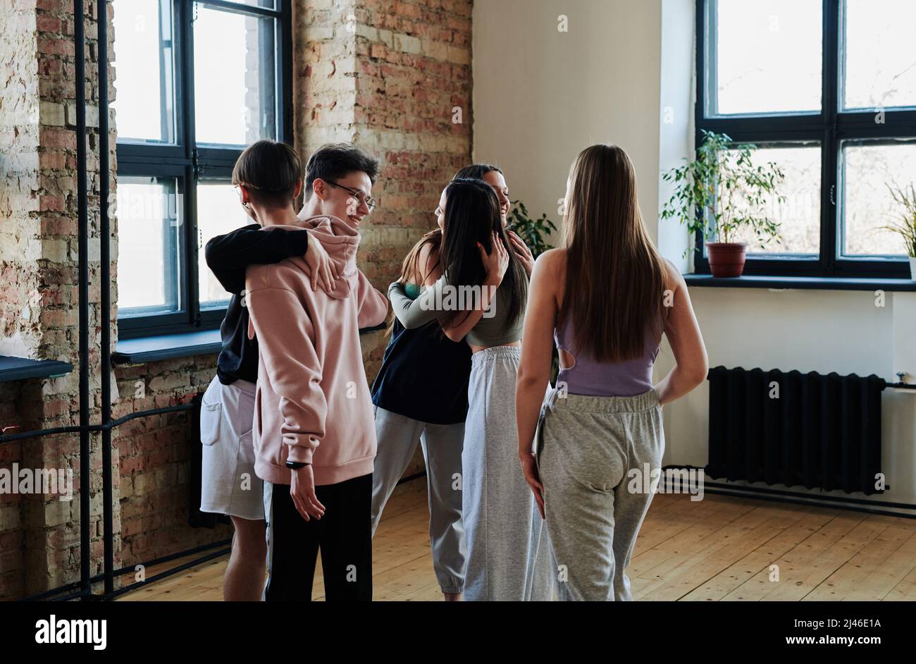 Gruppo di ragazzi e ragazze adolescenti felici in abbigliamento sportivo dando abbracci l'uno all'altro prima di ripetizione in studio moderno di coreografia Foto Stock