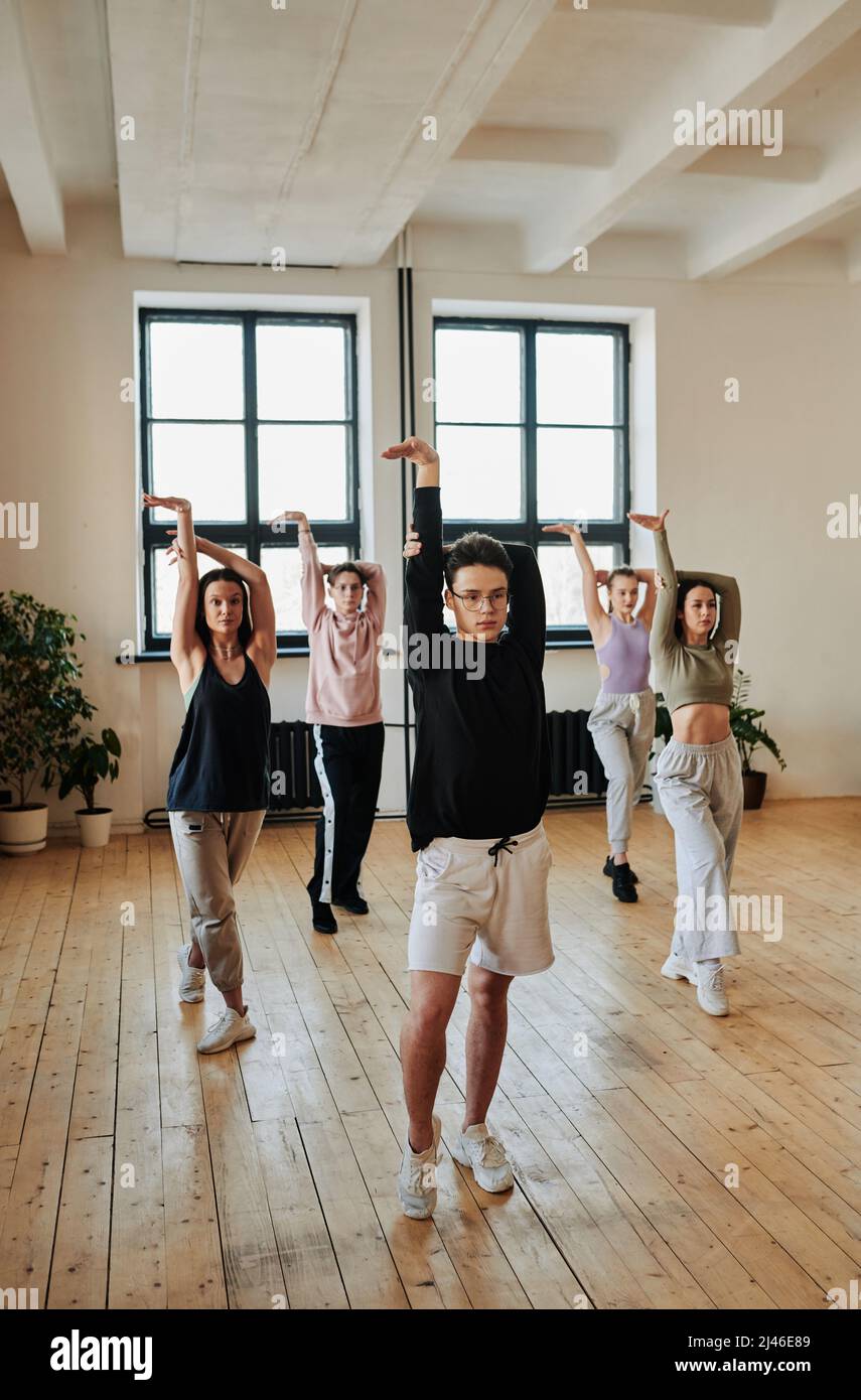Giovane teenage leader maschile del gruppo di performance che mostra esercizi di danza voga per gruppo di ragazze e ragazzo durante l'allenamento in studio Foto Stock