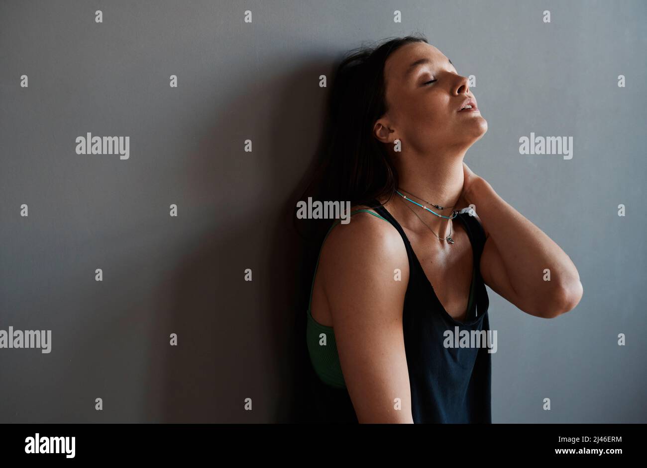 Giovane ballerina di vogue femminile stanca o altra performer in nero Tantop in piedi da parete grigia di studio loft a pausa e di riposo Foto Stock