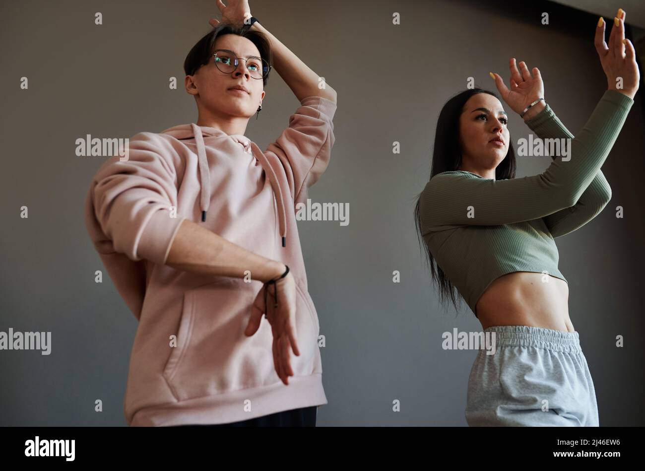 Ragazzo e ragazza teenage attiva contemporanea con braccia sollevate che ballano in voga durante la ripetizione contro il muro grigio in studio Foto Stock