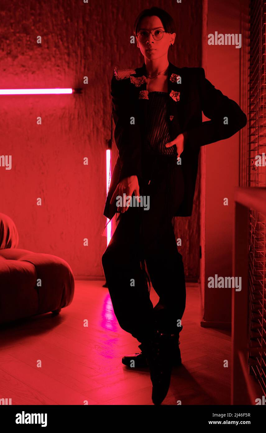 Giovane uomo elegante in astuto abbigliamento nero che esegue movimenti di danza vogue nella sala di illuminazione rossa del club di intrattenimento contemporaneo Foto Stock