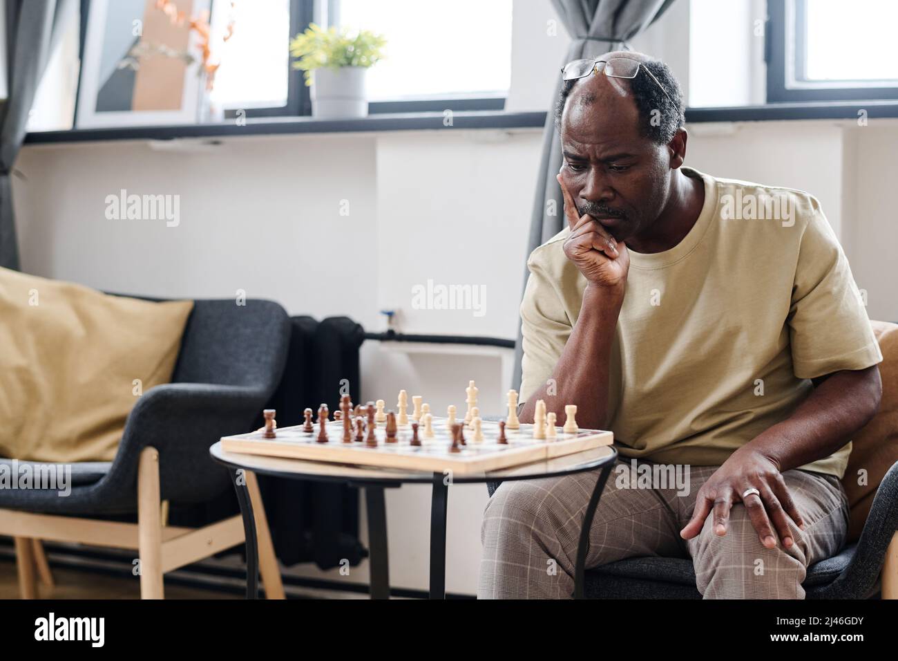 Pensionato pensionato uomo di etnia africana guardando la scacchiera su una piccola tavola rotonda mentre si pensa alla prossima mossa Foto Stock
