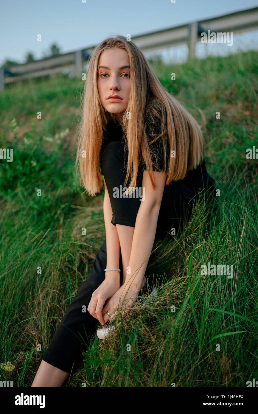 donna dai capelli lunghi seduta sull'erba Foto Stock