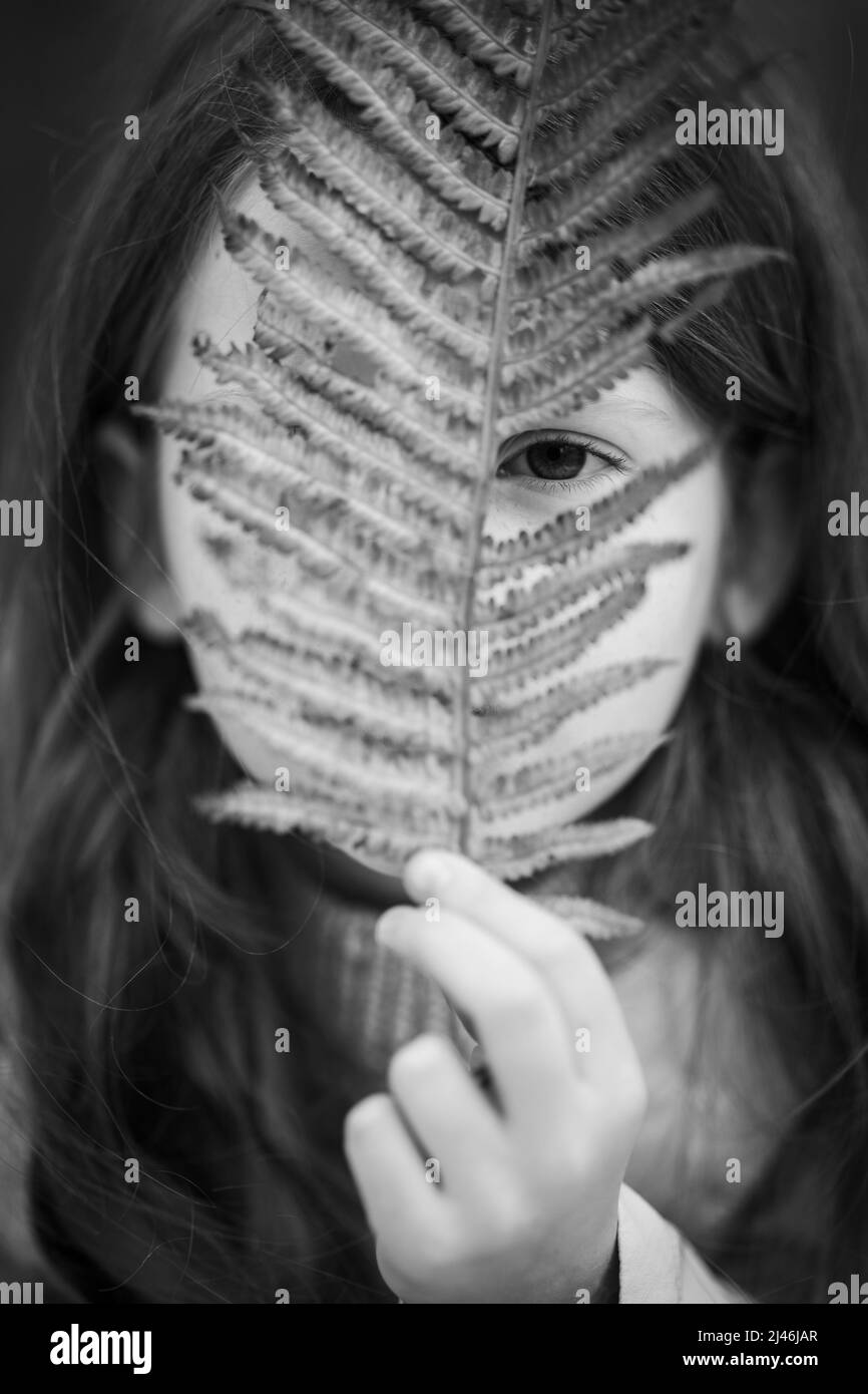 Una ragazza pensierosa con gli occhi marroni guarda attraverso un ramo di una felce. Foto Stock