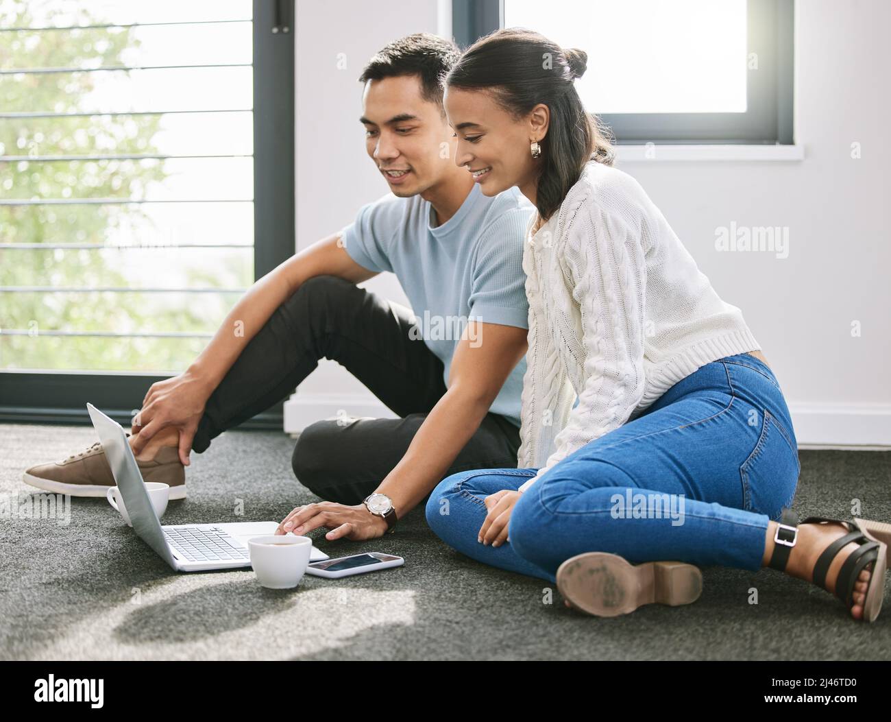 Volevo mostrarti i mobili che ho appena ordinato. Scatto di una giovane coppia seduta sul pavimento insieme nella nuova casa e utilizzando un computer portatile. Foto Stock