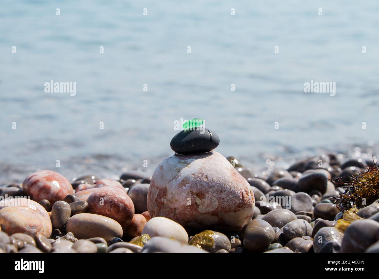 La piramide è costruita su una spiaggia di ciottoli di mare con un vetro verde satinato liscio in cima. Sullo sfondo di onde, schizzi d'acqua e. Foto Stock