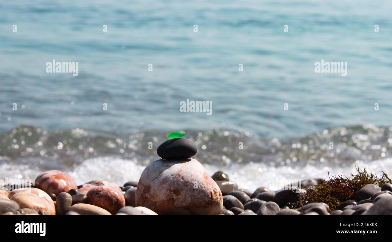 La piramide è costruita su una spiaggia di ciottoli di mare con un vetro verde satinato liscio in cima. Sullo sfondo di onde, schizzi d'acqua e. Foto Stock