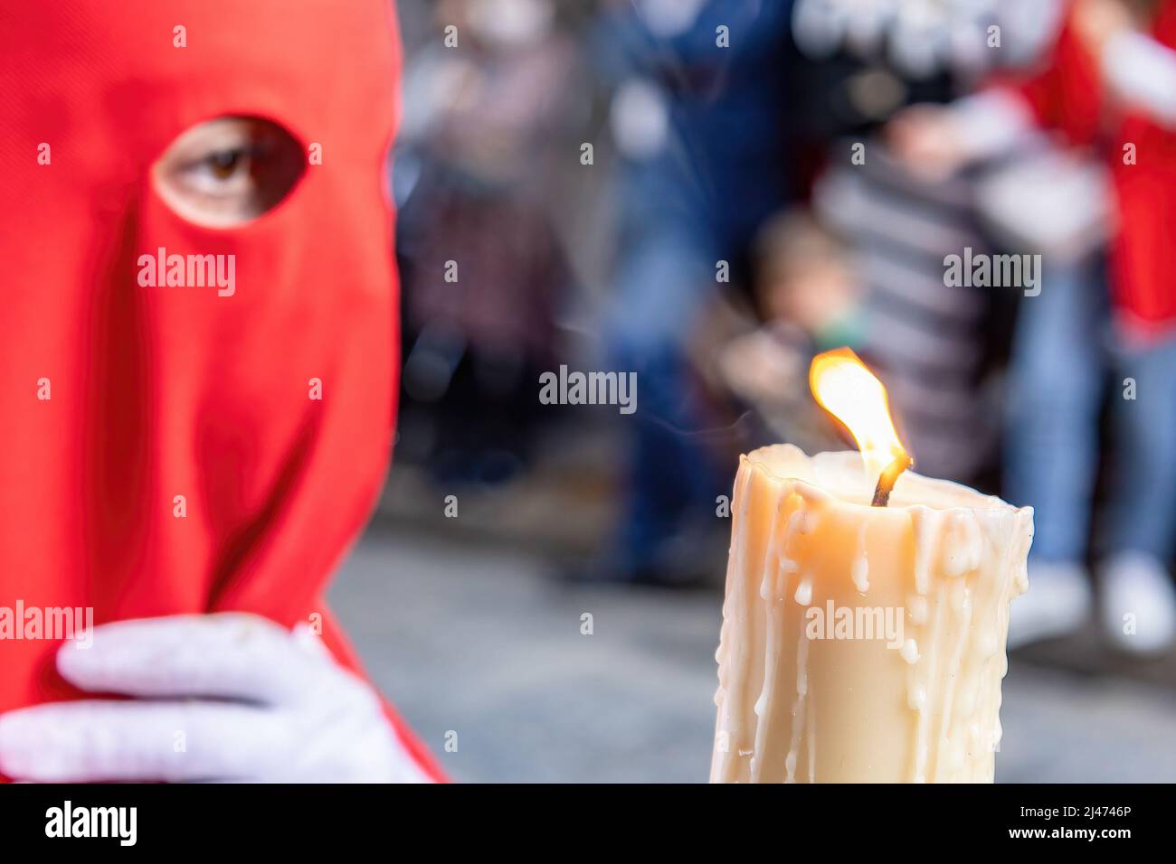 La candela in fiamma di un giovane Nazareno con un cappuccio rosso che fa la sua stazione di penitenza nella processione della settimana Santa. Fuoco selettivo solo con fiamma candela Foto Stock