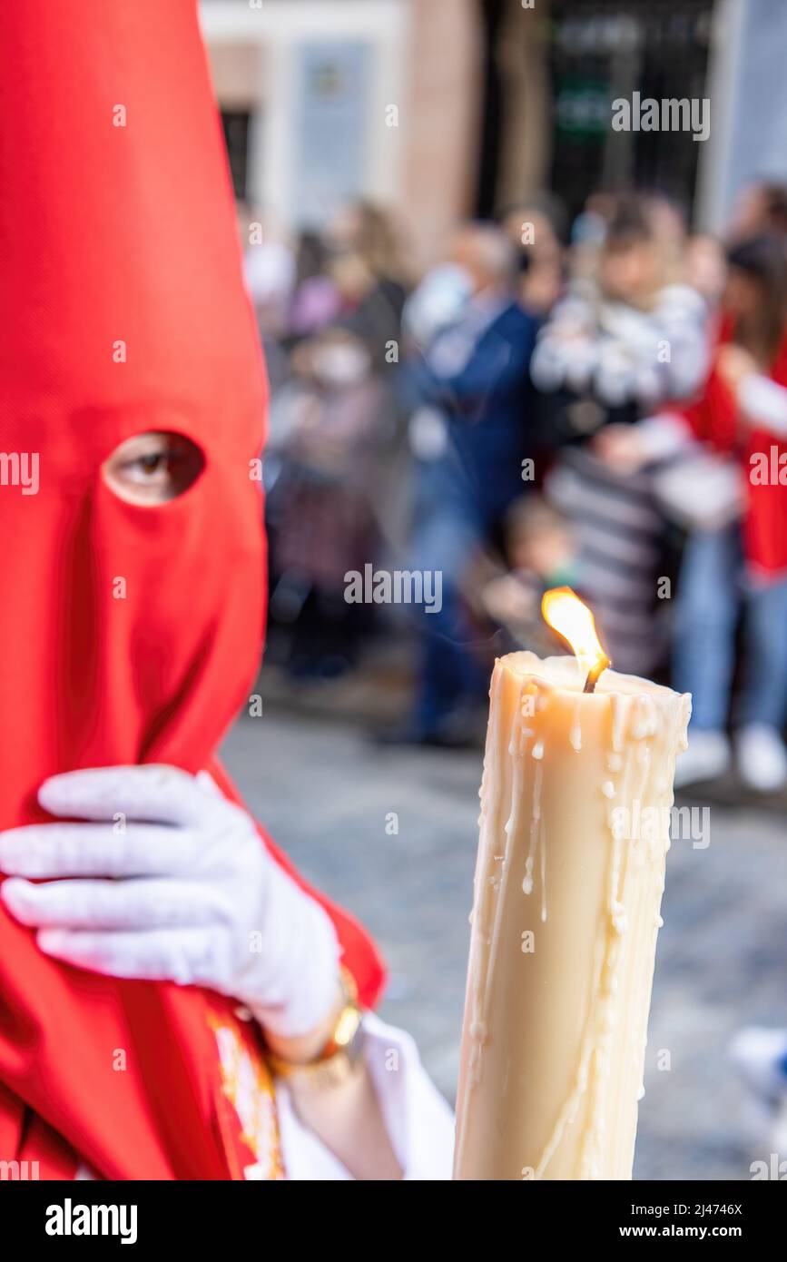 La candela in fiamma di un giovane Nazareno con un cappuccio rosso che fa la sua stazione di penitenza nella processione della settimana Santa. Fuoco selettivo solo con fiamma candela Foto Stock