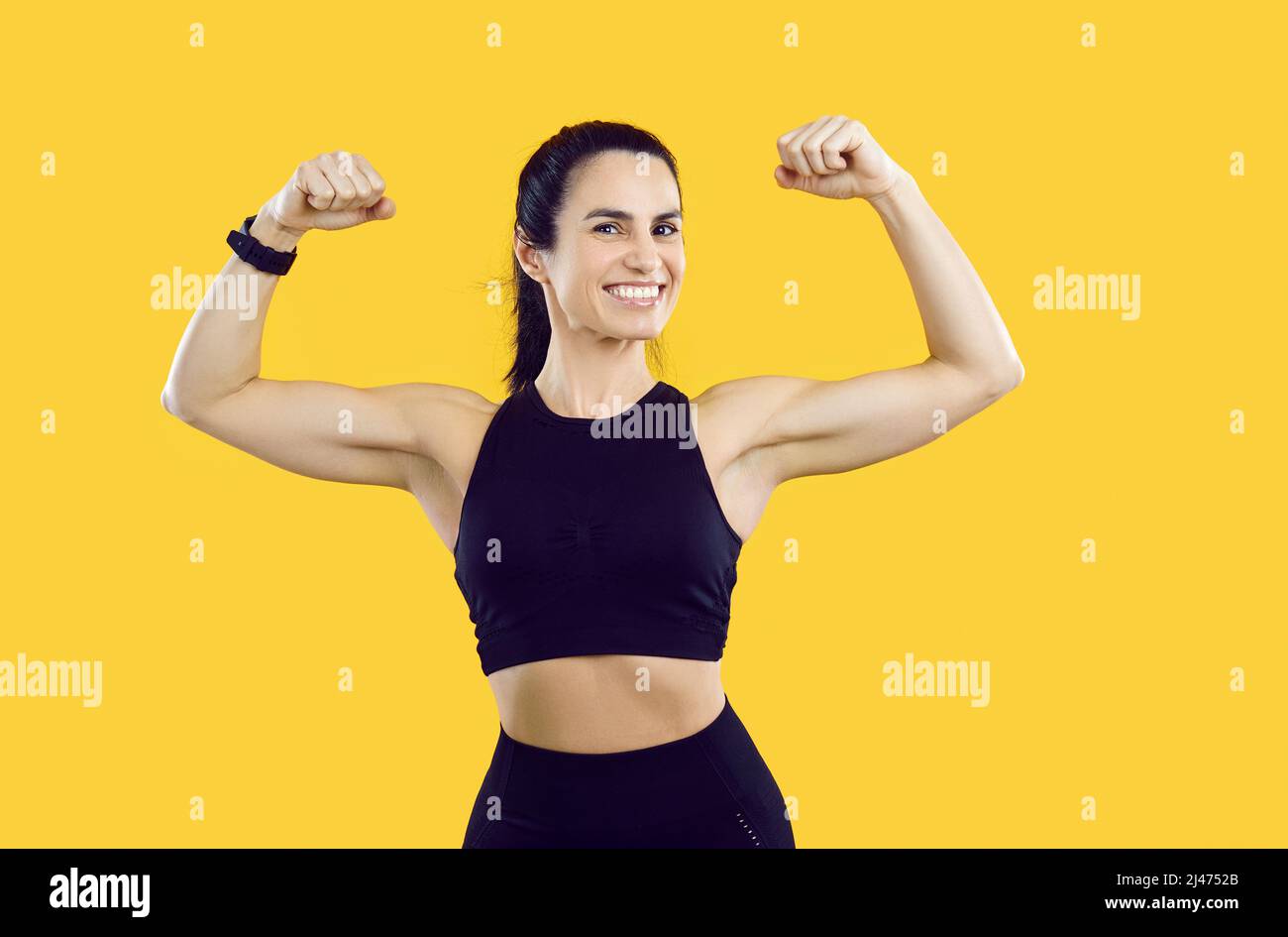 Studio girato di atleta felice femmina mostrando i suoi muscoli bicep forte e sorridente Foto Stock