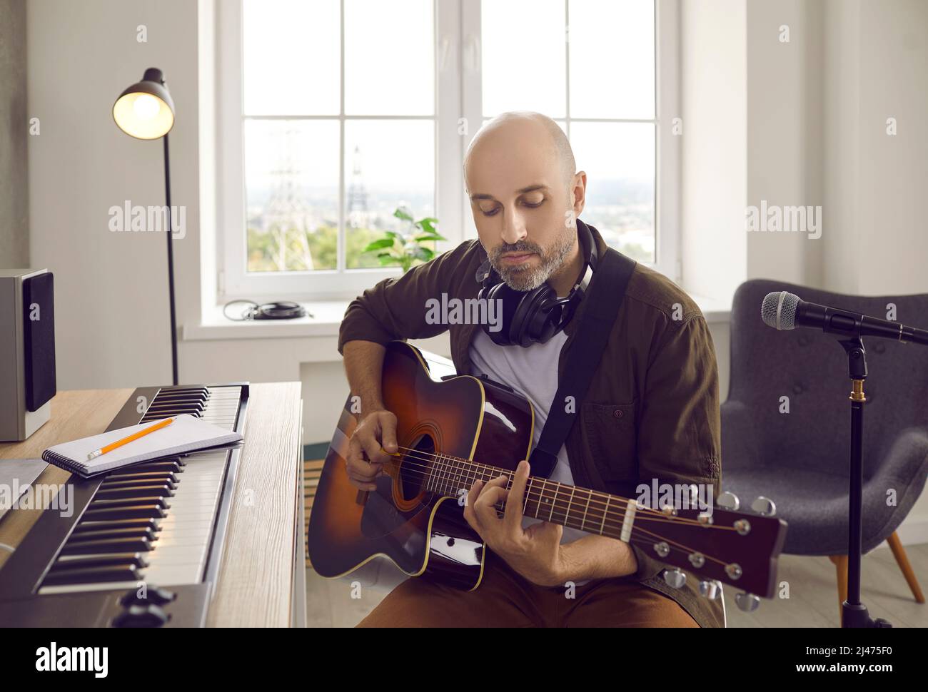 Songwriter e chitarrista suonano la chitarra mentre si siede a tastiera elettronica in casa studio Foto Stock