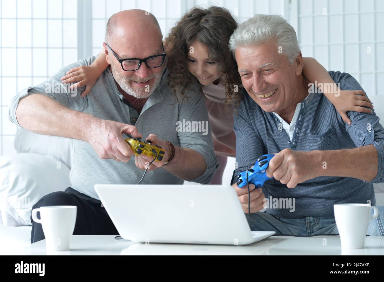 Uomini anziani con nipote che giocano a un videogame per computer portatile a casa Foto Stock