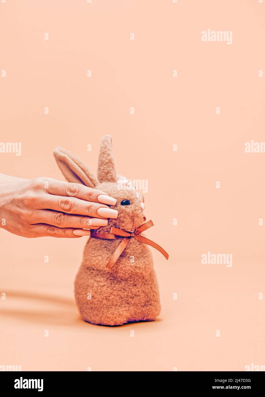 Un concetto di Pasqua creativo e insolito. Le mani femminili nascondono gli occhi di un piccolo coniglietto di Pasqua marrone soffuso. Aspetto estetico realistico. Stile contemporaneo. B Foto Stock