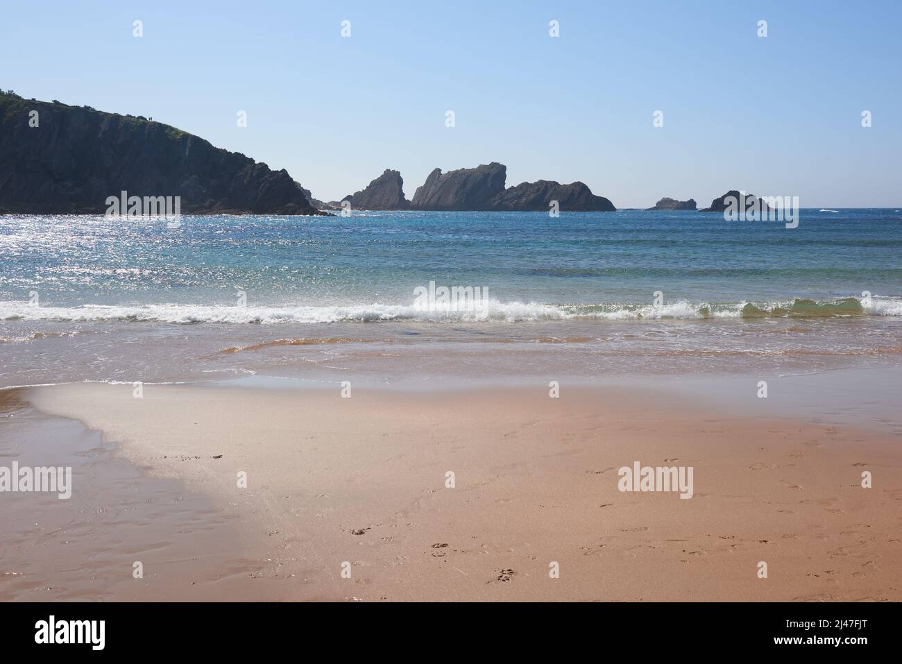 Una tranquilla spiaggia di sabbia fine con scogliere sullo sfondo Foto Stock