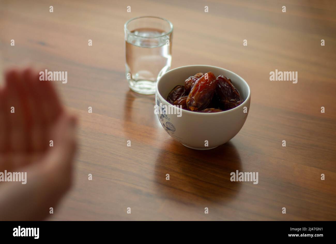 Ramadan o concetto di iftar per i musulmani. La persona sta pregando con le mani prima di rompere il digiuno. Medjool, acqua, pasto minimo su tavolo da pranzo in legno. Bail M Foto Stock