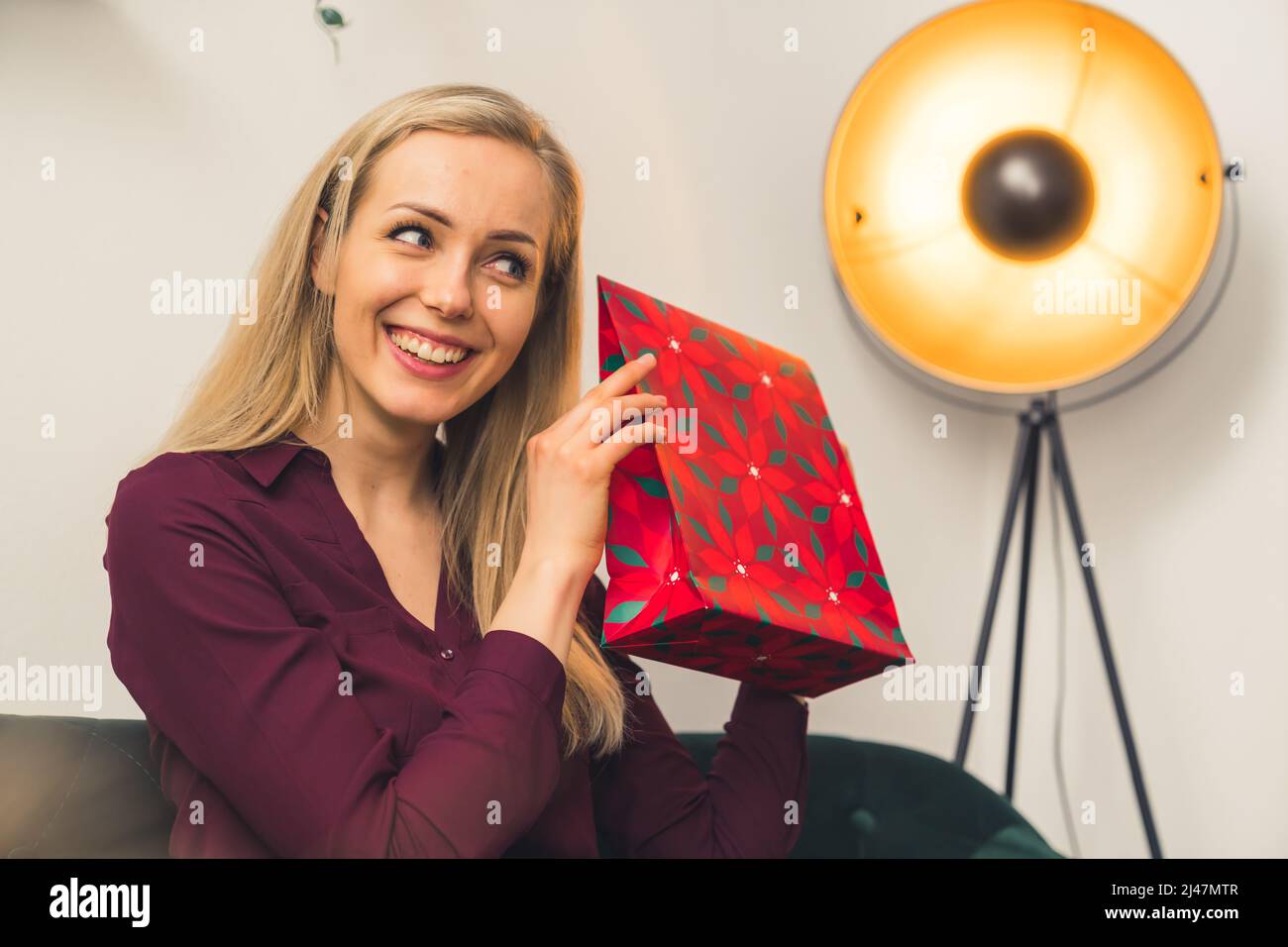 È il momento di aprire regali - una ragazza bionda europea attraente che tiene un regalo e sorridente medio primo piano studio girato in interni benessere concetto. Foto di alta qualità Foto Stock