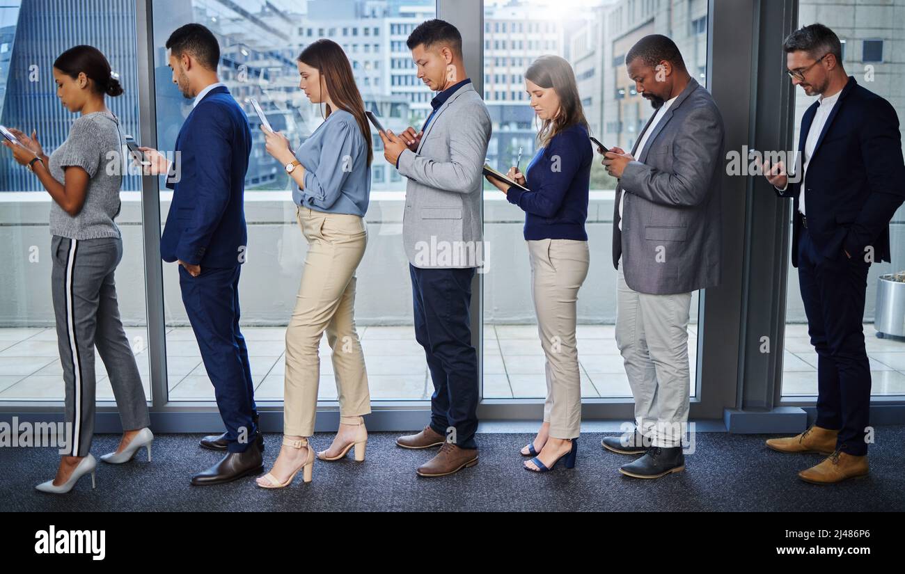 Il successo viene dalla preparazione. Scatto di un gruppo di giovani imprenditori che utilizzano dispositivi digitali mentre attendono in linea. Foto Stock