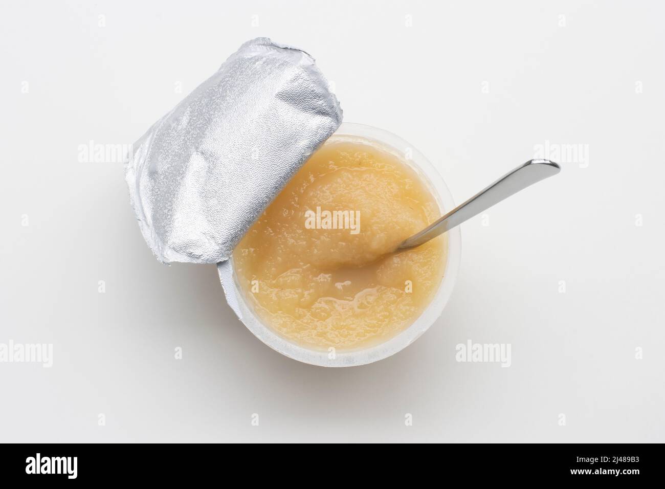 Vista dall'alto di una tazza aperta di salsa di mele non zuccherata con un cucchiaio, isolata su sfondo bianco. Snack vegano senza glutine per bambini. Foto Stock