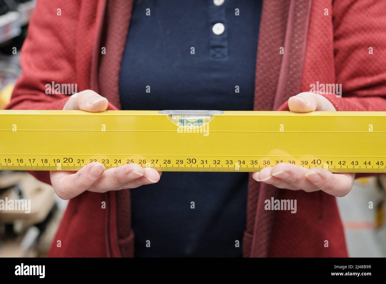 La donna in negozio sceglie il livello da acquistare per determinare l'orizzonte liscio. Le mani si avvicinano Foto Stock