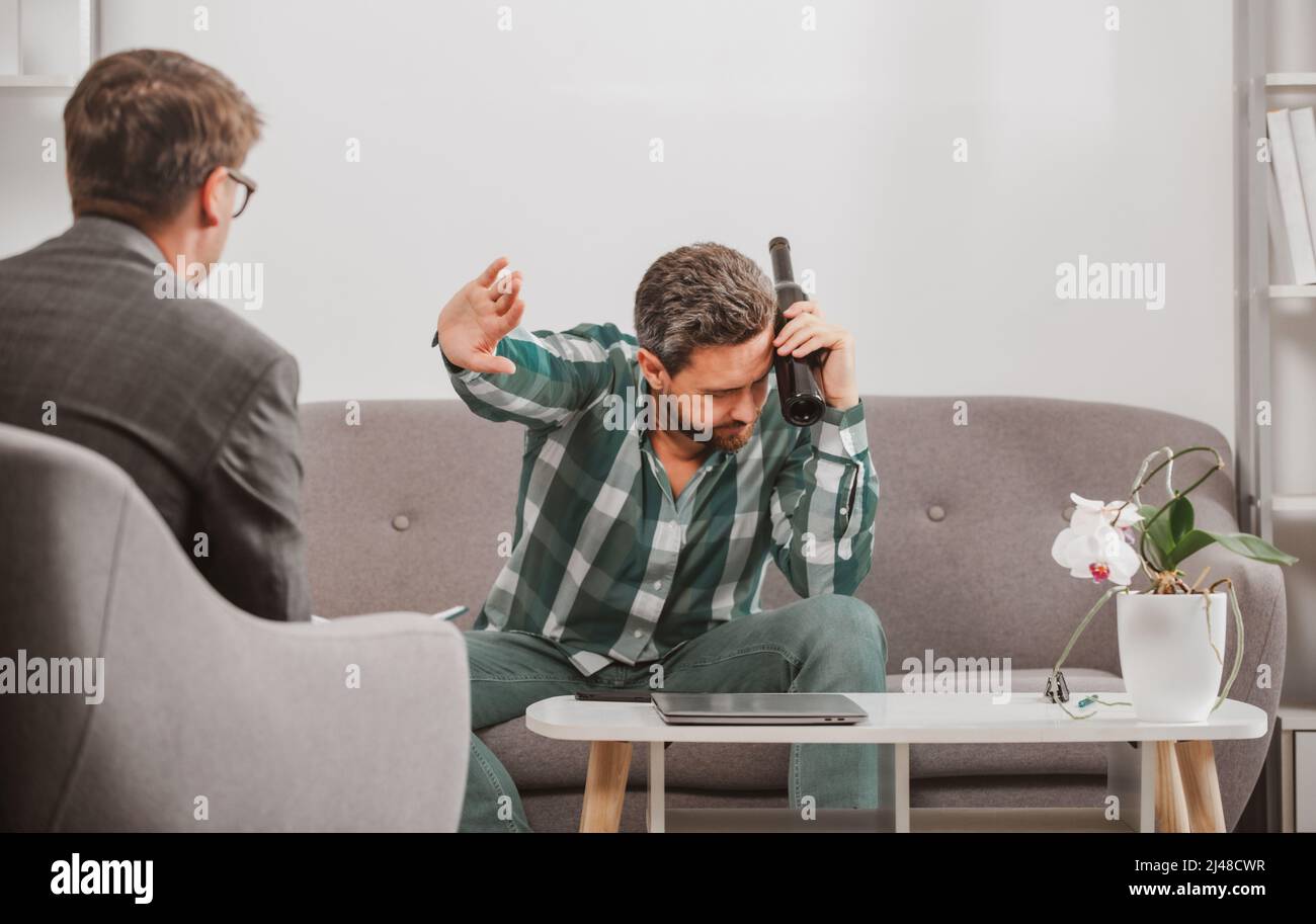 Uomo depresso con bottiglia di vino in sessione di psicoterapia. Abuso delle persone e problemi di alcolismo. Psicologia, concetto di terapia mentale. Foto Stock