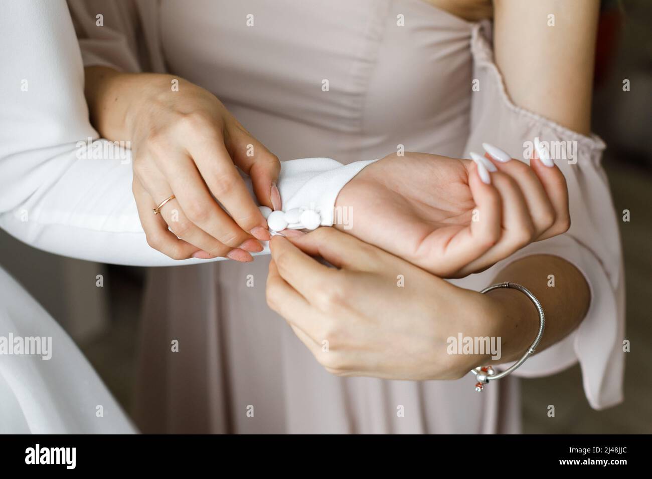 La ragazza aiuta la sposa a indossare un abito da sposa abbellendo le maniche. Foto Stock