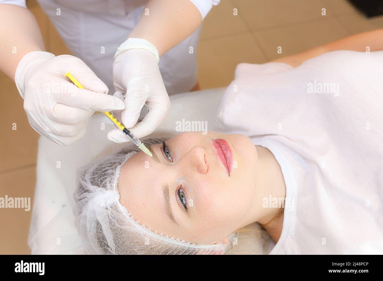 Un cosmetologo esegue una procedura di ringiovanimento facciale iniettando le iniezioni per lisciare le rughe nella zona della fronte Foto Stock