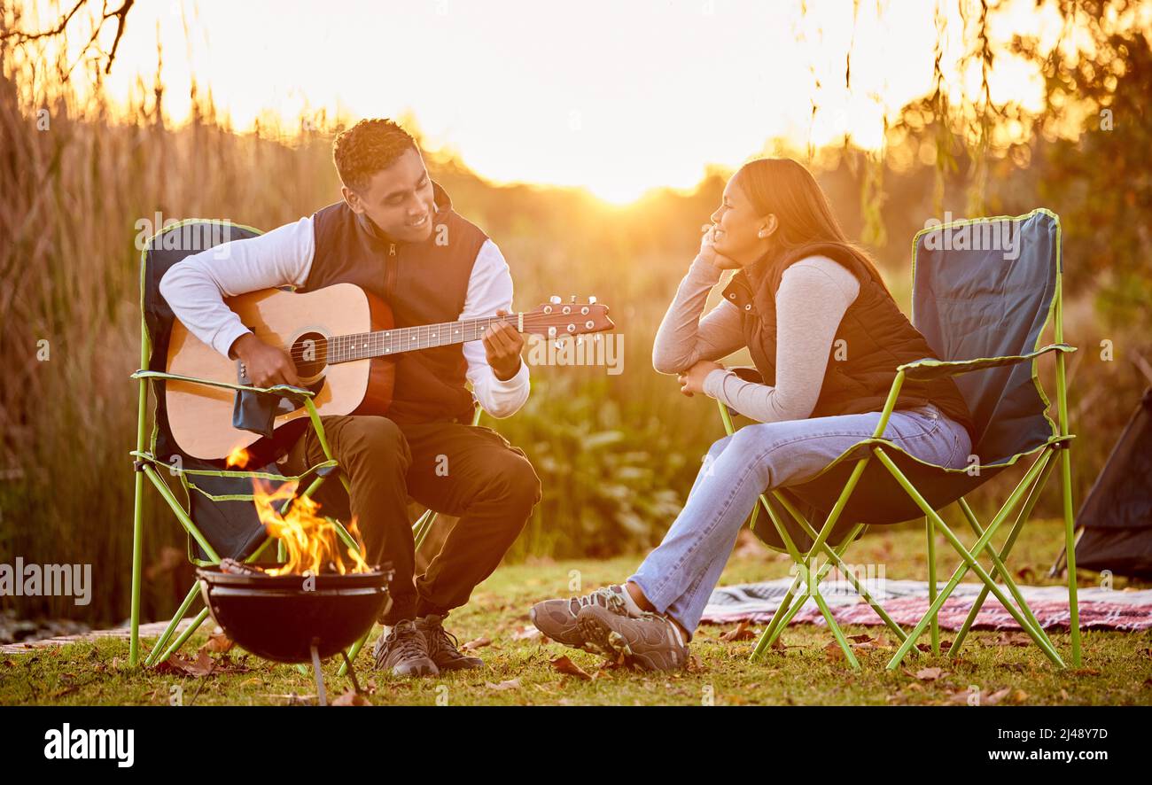 La vita è migliore intorno al fuoco del campeggio. Scatto di un tu che suona la sua chitarra a sua moglie fuori mentre campeggio. Foto Stock