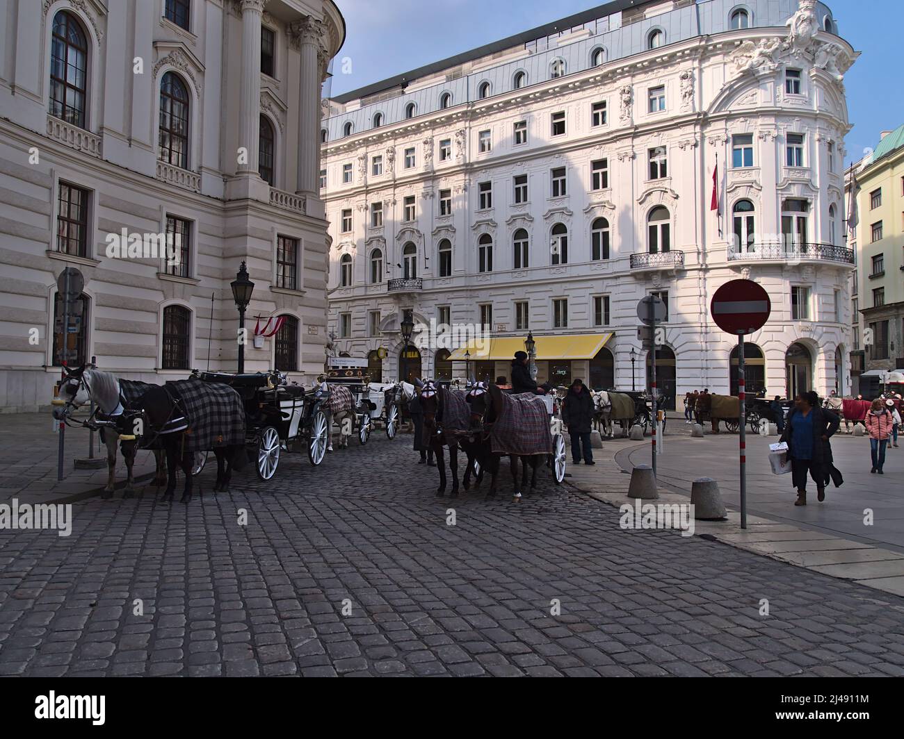 Scena affollata nella famosa piazza Michaelerplatz nel centro storico di Vienna, Austria, con carrozze trainate da cavalli in attesa di turisti. Foto Stock