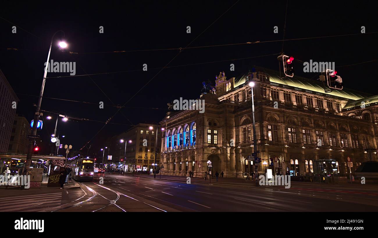 Splendida vista sulla facciata illuminata dell'edificio dell'Opera di Vienna in Austria di notte con tram di fronte. Foto Stock