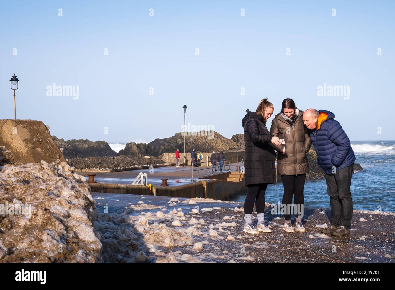 Un gruppo di persone che si godono il sole del tempo invernale al porto di Ballintoy in Co. Antrim Irlanda del Nord. Foto Stock