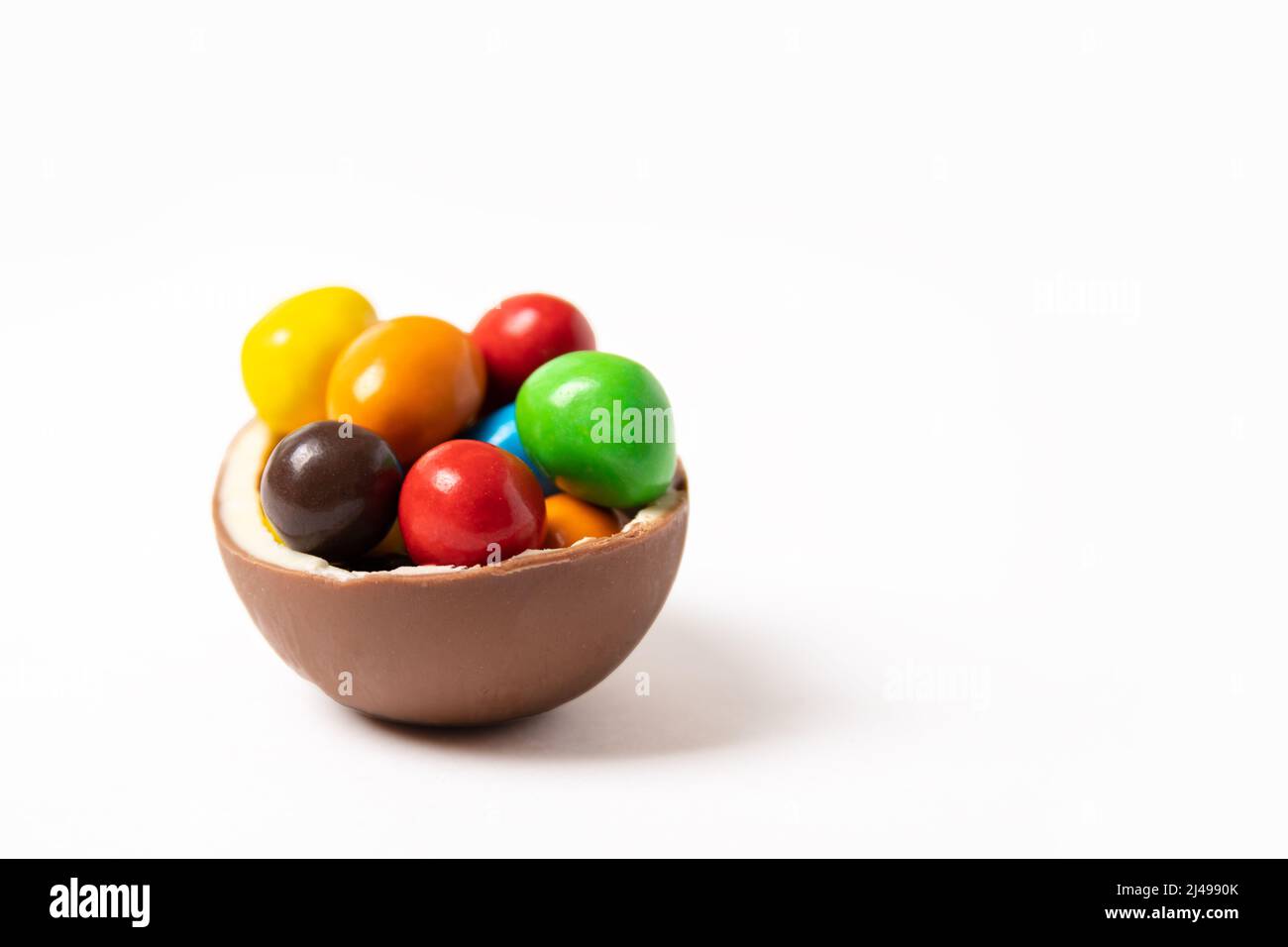 Uovo di pasqua al cioccolato cracked con piccole caramelle colorate rotonde su sfondo bianco, spazio copia, vista laterale. Cioccolatini per bambini. Concetto di Pasqua. Foto Stock
