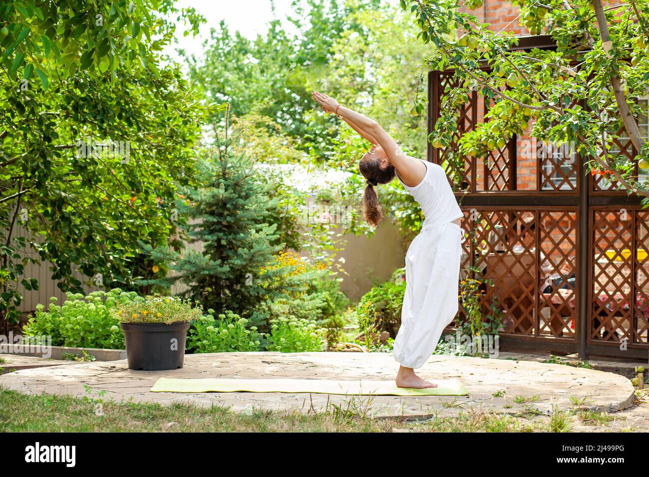 La giovane donna pratica lo yoga in giardino. Deflessione nella pratica di surya namaskar. Tadasana - posa in montagna con mani distese Foto Stock