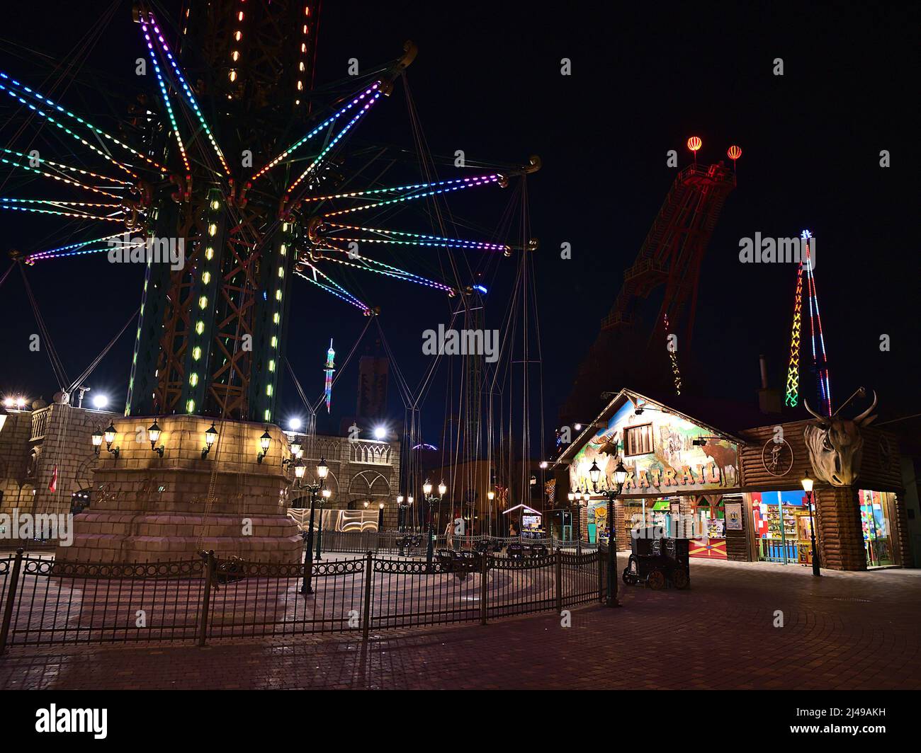 Vista notturna del famoso parco divertimenti Wurstelprater a Vienna, Austria, con torre di lancio illuminata e negozi in serata. Foto Stock