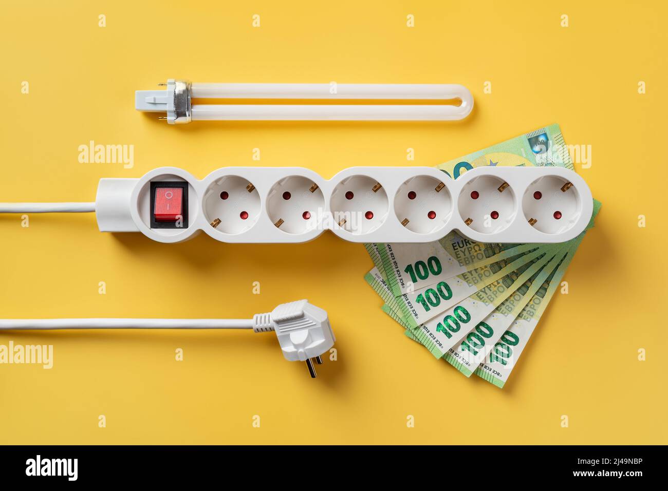 Presa multipla su banconote da 100 euro, spina elettrica e lampadina fluorescente su sfondo giallo. Aumento dei costi di illuminazione, riscaldamento e raffreddamento. Foto Stock