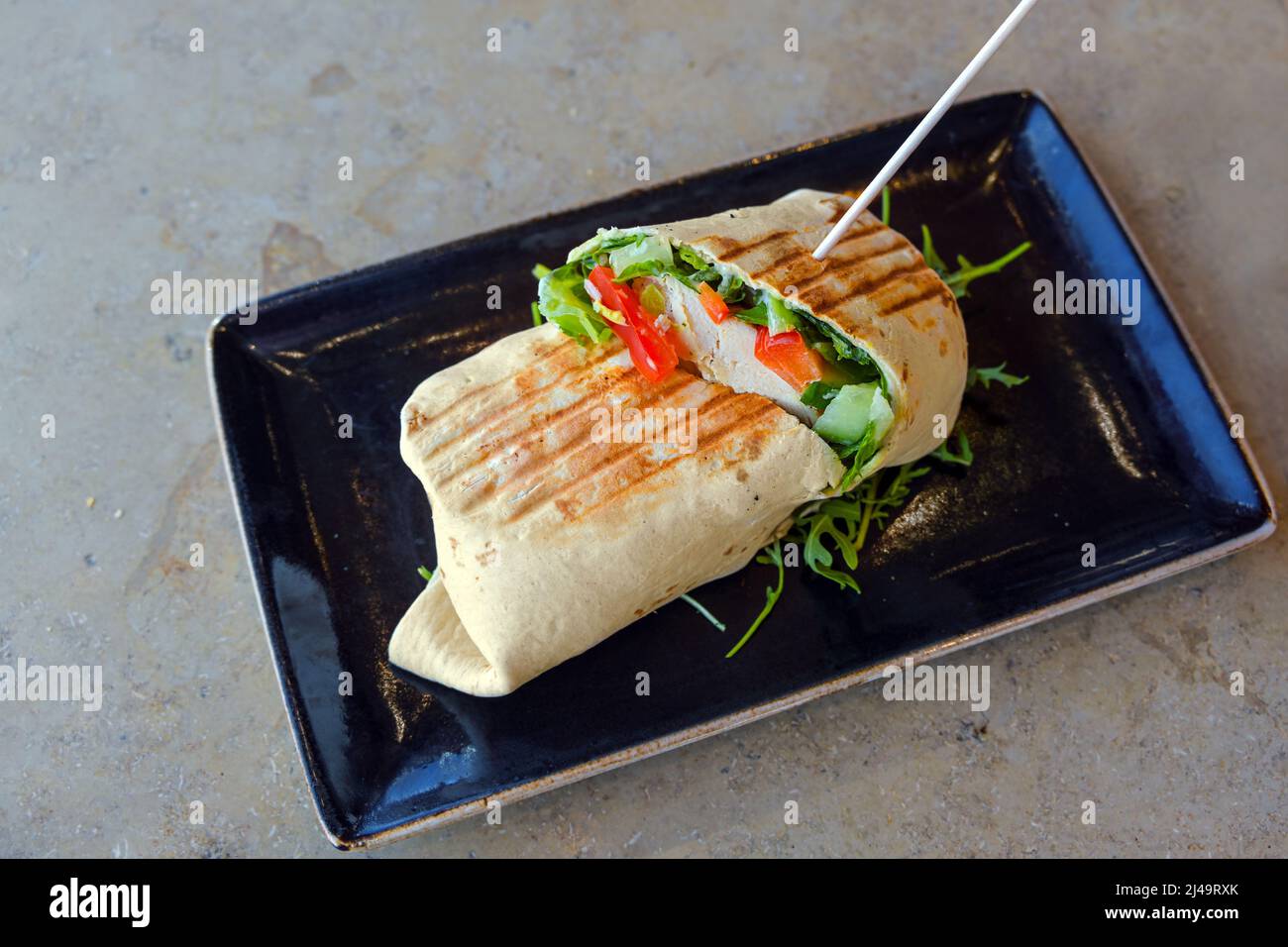 Tortilla wrap riempito con pollo e verdure su un piatto nero e un tavolo di marmo, cibo messicano, spazio copia, fuoco selezionato, stretta profondità di campo Foto Stock